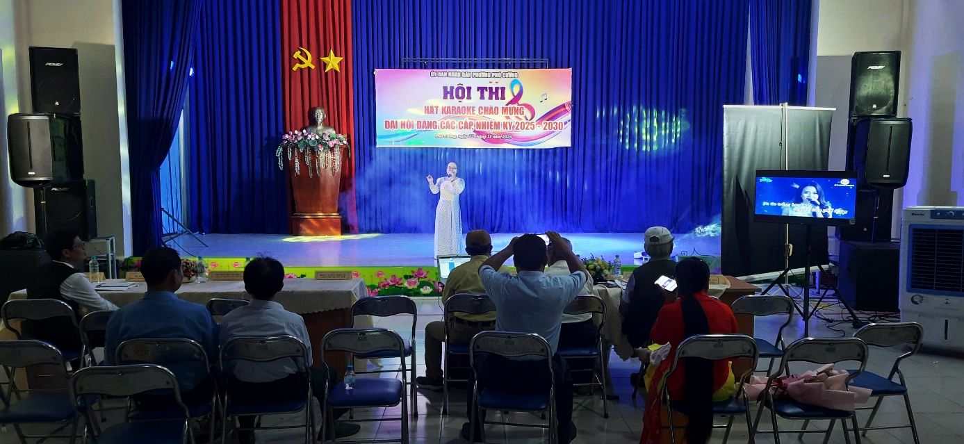 A person on stage with people sitting in chairsDescription automatically generated
