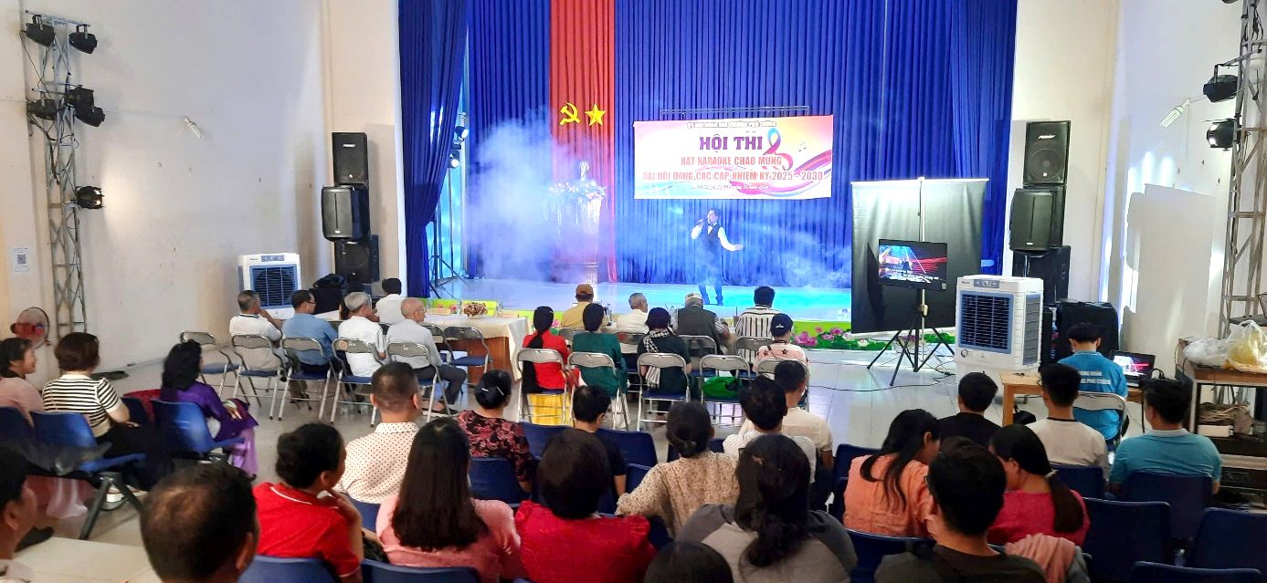 A group of people sitting in a room with a stage and a stage with a screenDescription automatically generated