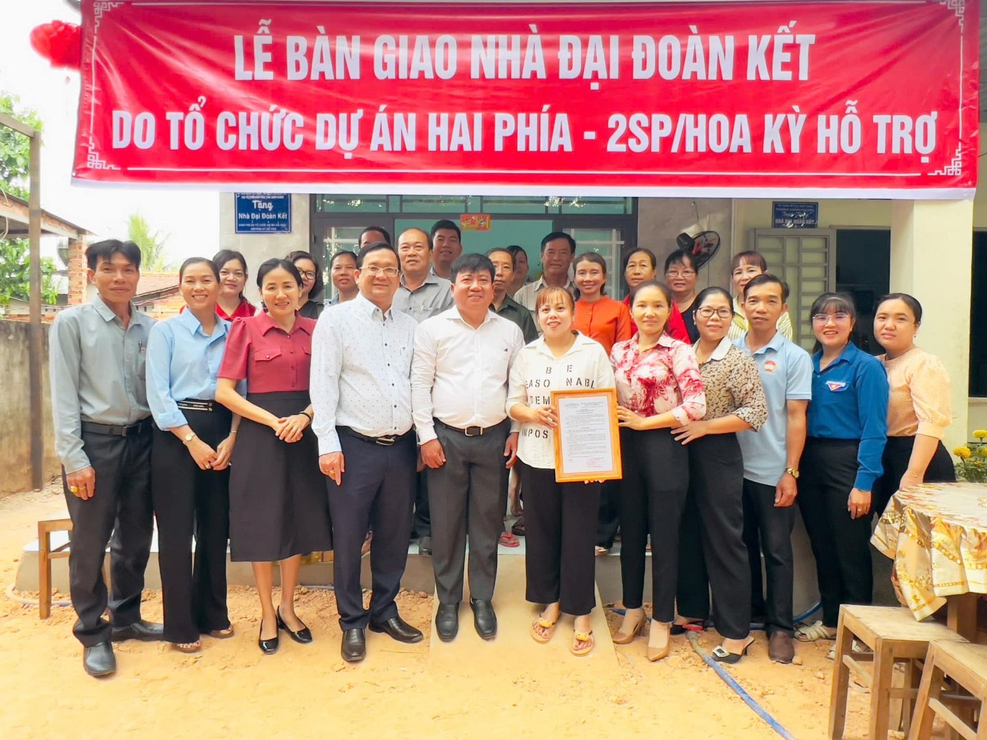 Có thể là hình ảnh về 10 người và văn bản cho biết 'LỄ BÀN GIAO NHÀ ĐẠI ĐOÀN KẾT DO TỔ CHỨC DỰ ÁN HAI PHÍA 2SP/HOA KỲ HỖ TRƠ อินโค. ಮಕ ASO MABL sNARL ABL TEM 토 I سا MPOS'